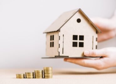 crop-hand-holding-house-near-coins